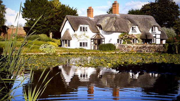 Photo of a thatched room cottage beside a lake.