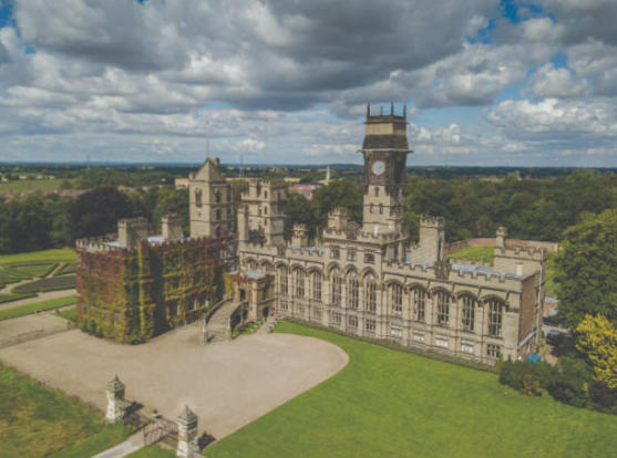 Aerial photo of a large castle with multiple wings and towers, the tallest of which is a clock tower. 